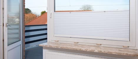 A room with a sliding glass door, a radiator, and a view of a neighboring building with a tiled roof.