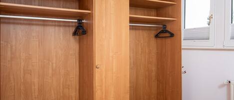 A wooden wardrobe with multiple shelves and hanging space, a small bench, and a window with blinds.