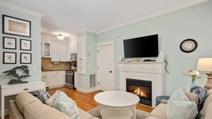 A living room with a fireplace, a television, and a kitchen in the background.