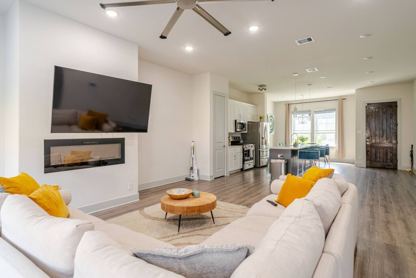 A modern living room with a white sofa, a wooden coffee table, and a flat-screen TV mounted on the wall.