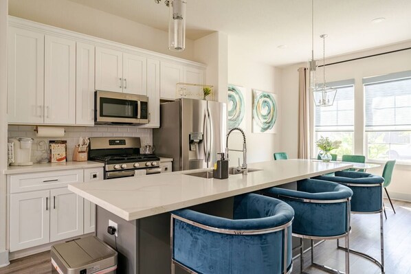 A modern kitchen with white cabinetry, stainless steel appliances, and a central island with bar stools. - Vibrant 3 Beds 2 bedroom House 15min from HOU (Houston)
