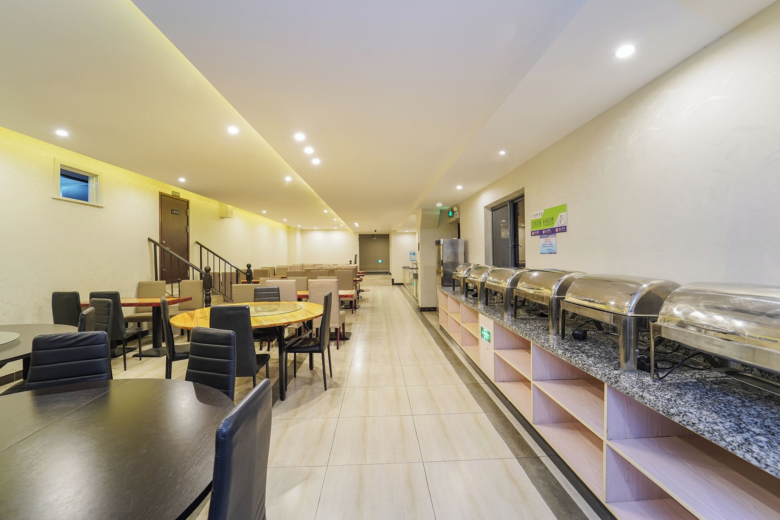A hotel dining area with tables, chairs, a buffet line, and a staircase.