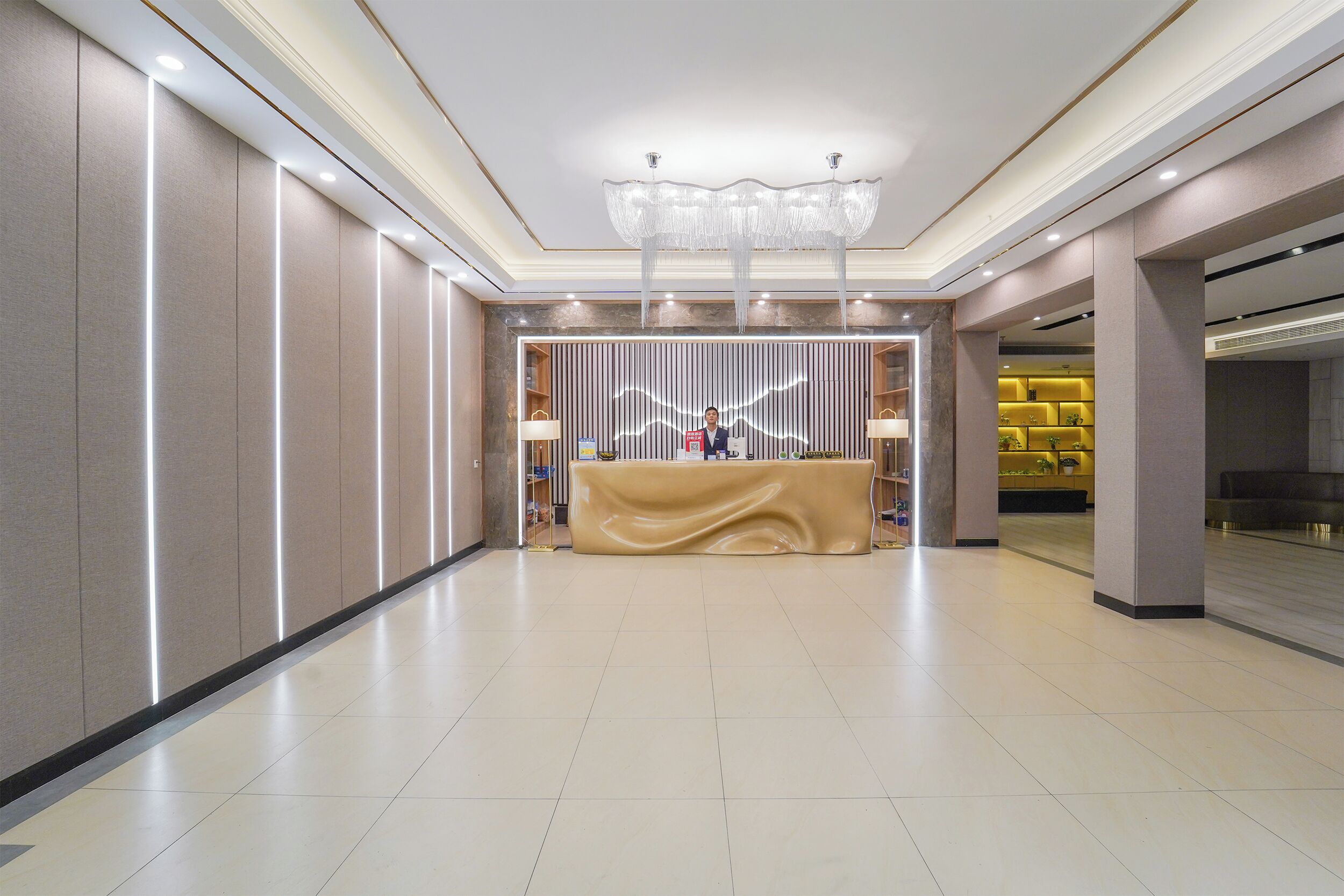 A spacious lobby with a reception desk, modern lighting, and a chandelier.