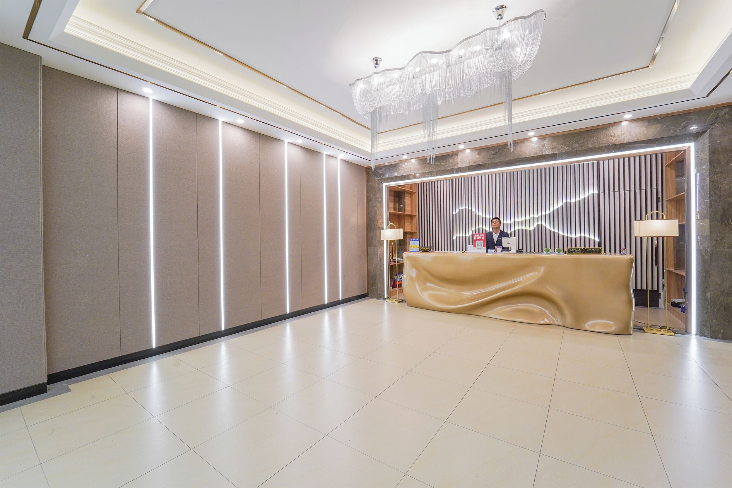 A hotel reception area with a modern design, featuring a reception desk, a chandelier, and a clean, tiled floor.