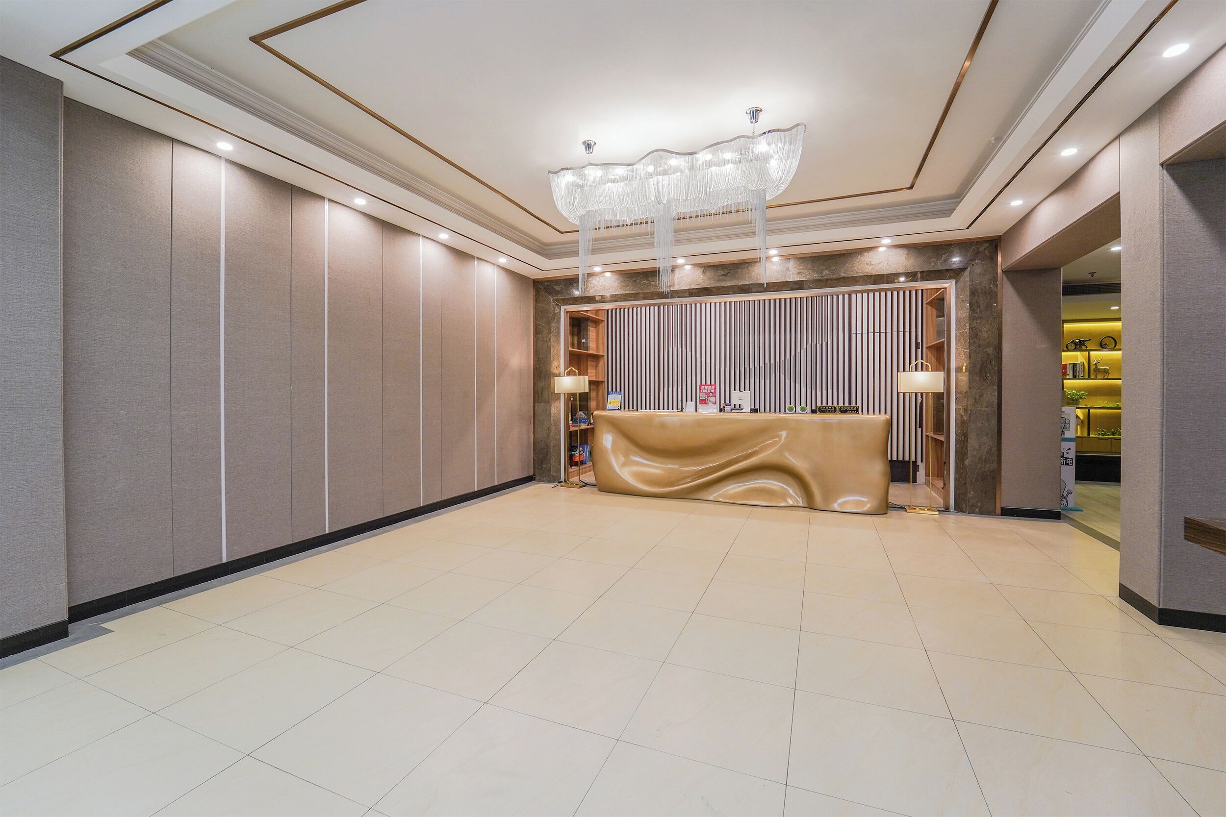 Een ruime lobby met een receptiebalie, inbouwverlichting en een decoratieve kroonluchter.