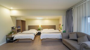 Habitación de hotel con dos camas, un sofá, una mesita de noche con lámpara y un armario.