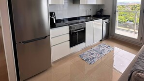 A modern kitchen with a stainless steel refrigerator, white cabinets, a black countertop, and a view of greenery through the window. - World Magic Vacaciones 5 (Cabanes)