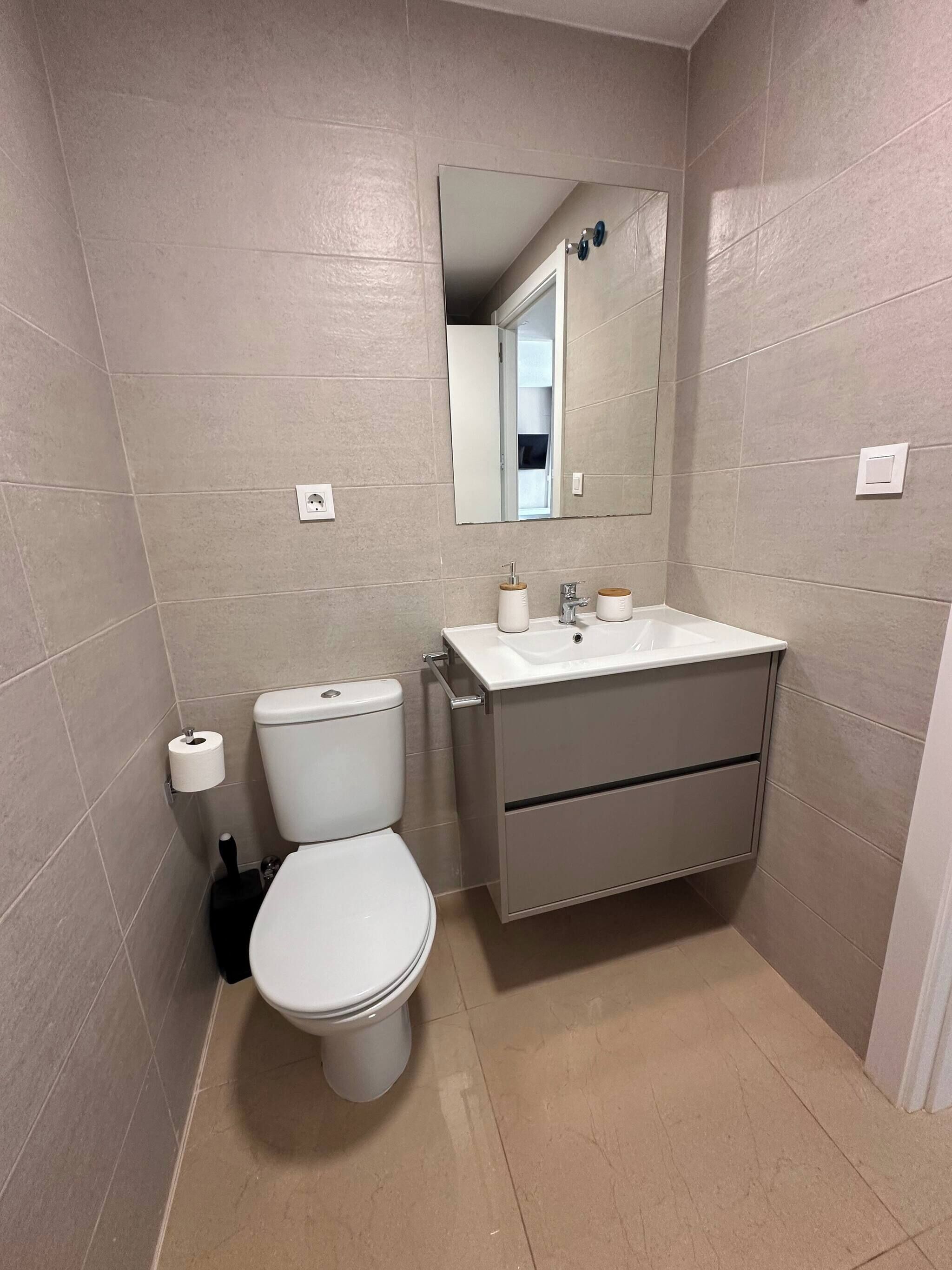 A bathroom with a toilet, sink, and mirror.