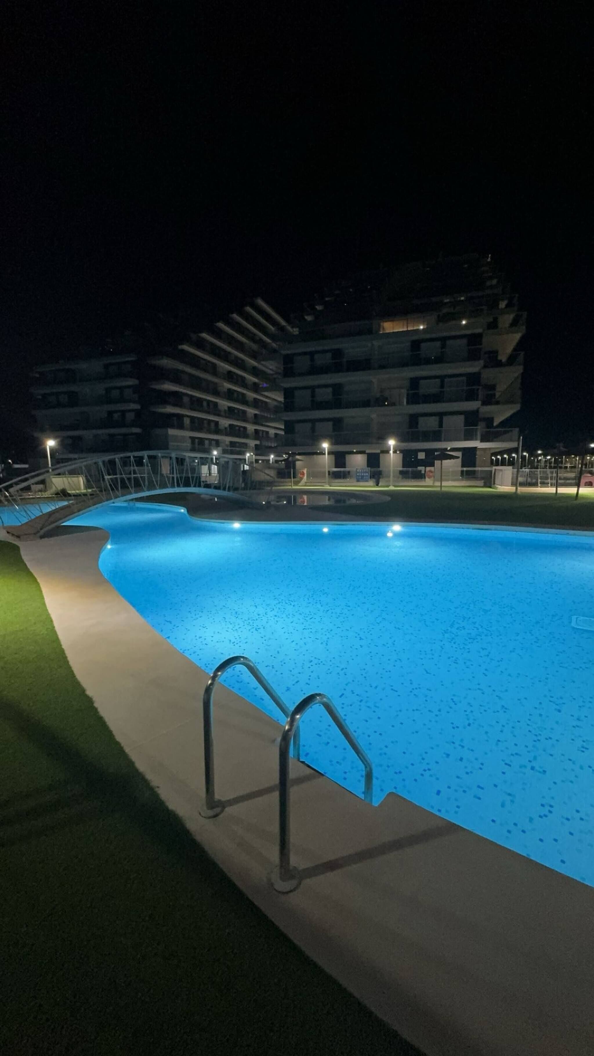 A swimming pool at night with a modern building in the background.