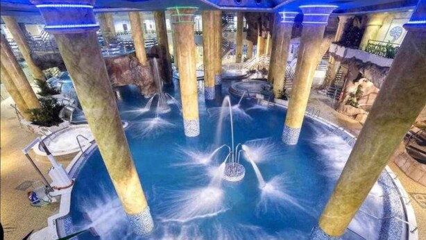 A circular water feature with multiple fountains, surrounded by columns and a pool. - World Magic Vacaciones 5 (Cabanes)