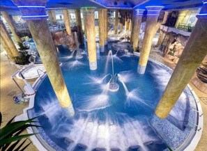 A circular water feature with multiple fountains, surrounded by columns and a pool. - World Magic Vacaciones 5 (Cabanes)
