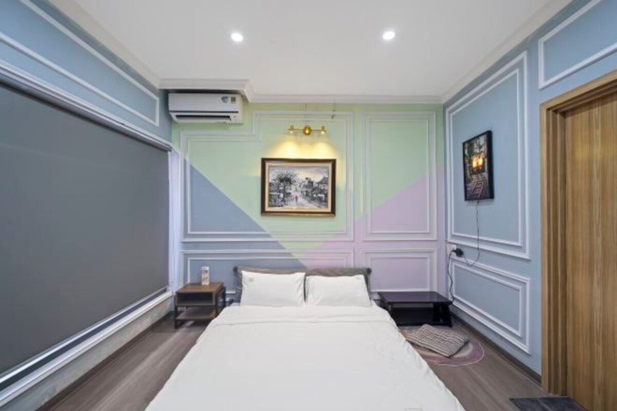 A bedroom with a bed, an air conditioning unit, a nightstand, a framed picture, and a door.