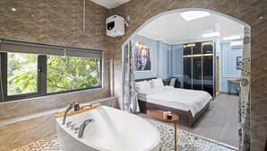 Un baño moderno con una bañera independiente, un ventanal grande y vistas a un dormitorio con cama y espejo.