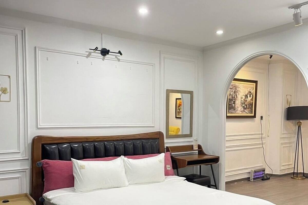 A modern bedroom with a wooden bed, white bedding, a desk, and a chair.