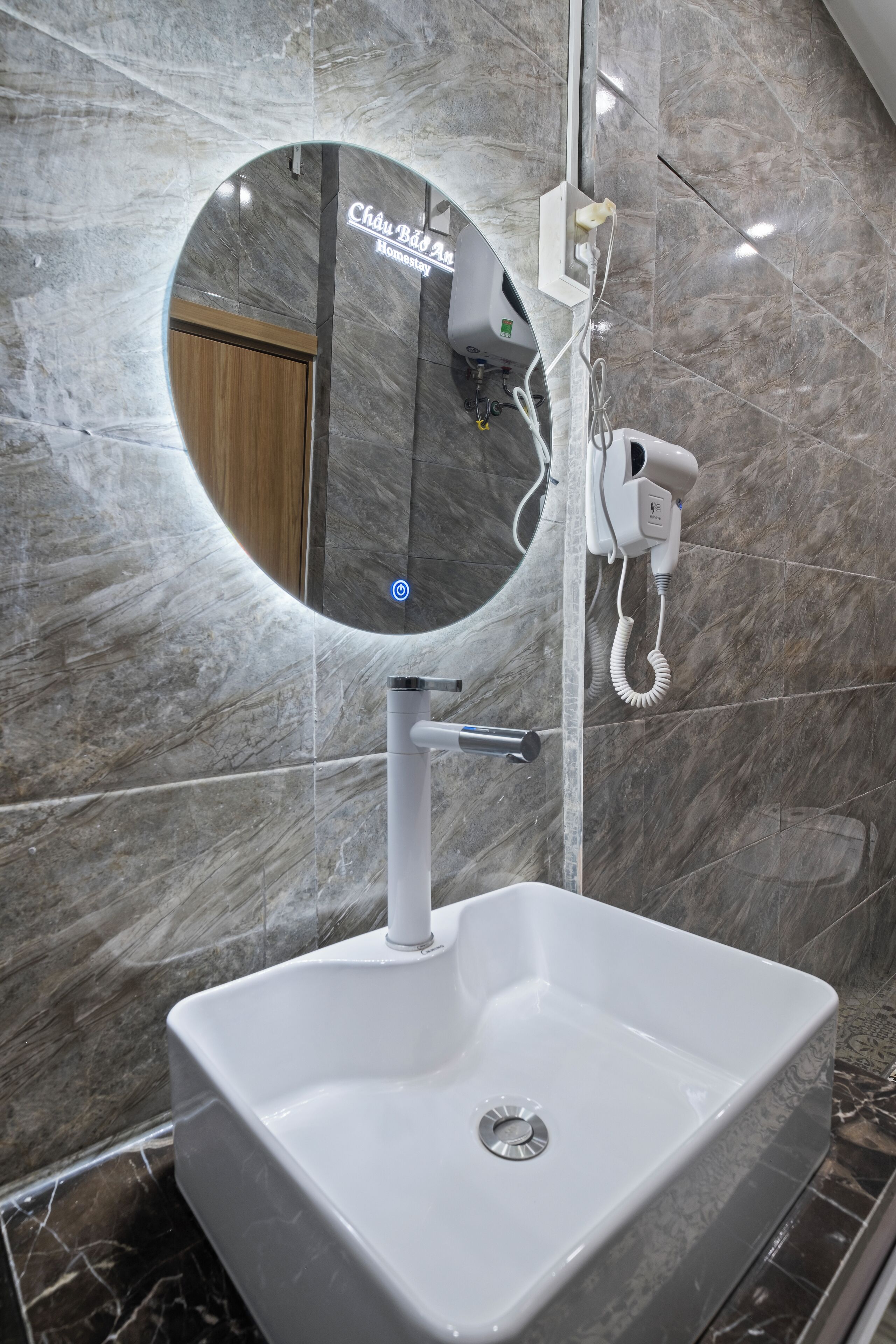 Une salle de bain avec un lavabo blanc, un miroir rond et un sèche-cheveux fixé au mur.