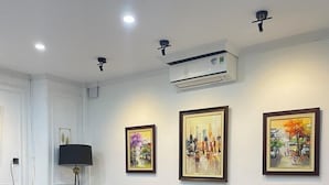 Una sala de estar moderna con un sillón amarillo, un pequeño reposapiés, un mueble bajo para televisión de madera y tres cuadros enmarcados en la pared.