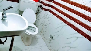 Kylpyhuone, jossa on valkoinen wc-istuin, pesuallas ja punavalkoraidallinen seinä.