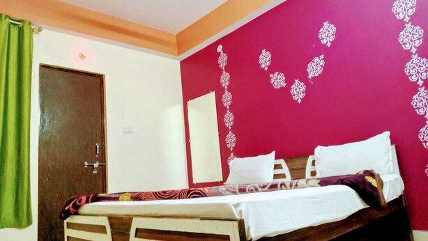 Un dormitorio con cama, una puerta y pared roja con motivos florales blancos.