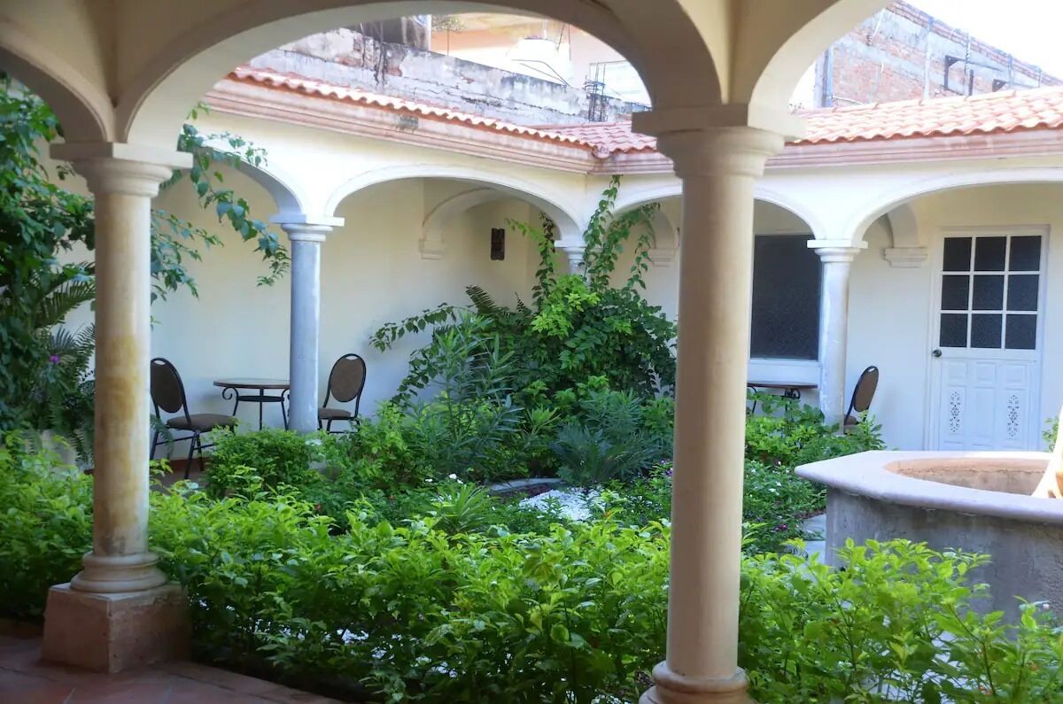 Un patio con arcos, una fuente y abundante vegetación.