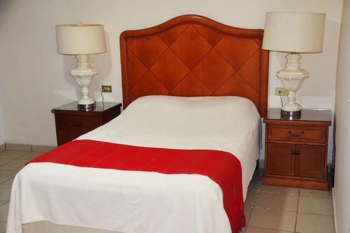 A bed with a red and white bedspread, two bedside tables with lamps, and a wooden headboard.