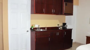 A compact kitchen with dark wooden cabinets, a white door, and a coffee maker on the counter. - Hotel Boutique Los Arcos (Los Mochis)
