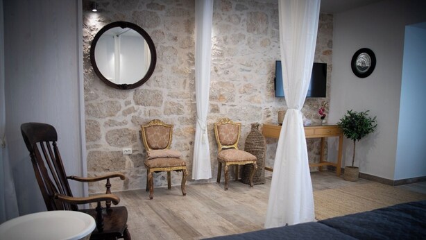 A room with a stone wall, two wooden chairs, a bed, a small table with a plant, and a mirror on the wall. - Harbour View House Studio Apartment  (Zaton)