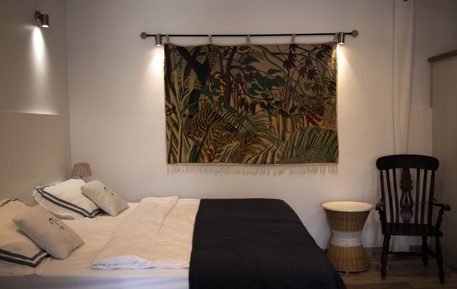 A bedroom with a bed, pillows, a tapestry, a chair, and a lamp.