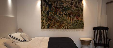 A bedroom with a bed, pillows, a tapestry, a chair, and a lamp.