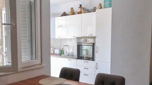 A dining area with a wooden table, four chairs, and three woven placemats. A kitchen with white cabinets and a stove is visible in the background. - Harbour View House Studio Apartment  (Zaton)