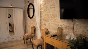 A room with a stone wall, a wooden desk, two upholstered chairs, a mirror, and a television. - Harbour View House Studio Apartment  (Zaton)