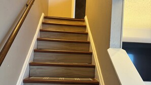 Una escalera de madera con un corredor de alfombra a rayas, paredes blancas y barandilla a la izquierda.