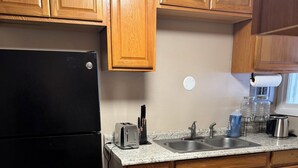 Una cocina con armarios de madera, un refrigerador negro, encimera de granito, un fregadero y una cafetera.