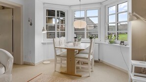 Un comedor con mesa y sillas de madera, ventanas grandes con contraventanas y una lámpara colgante.