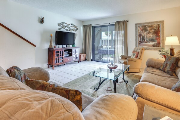 A living room with a sofa, a glass coffee table, a TV on a wooden cabinet, and a painting on the wall. - Riverfront Weleka Condo w/ Dock & Pool Access (Welaka)