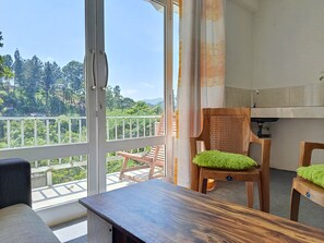 A balcony with a view of greenery and mountains, a wooden chair with a green cushion, and a wooden table. - C&D Ella (Ella)