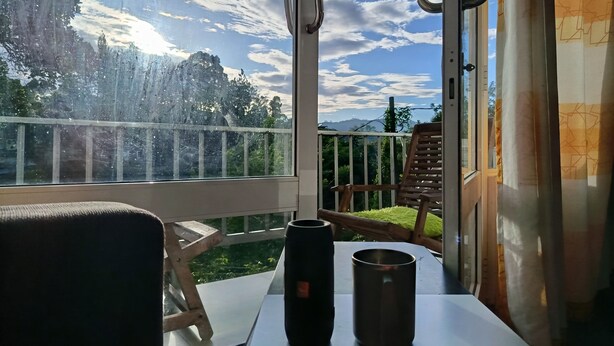 A balcony with a view of trees and mountains, a wooden chair, and a table with a mug. - C&D Ella (Ella)