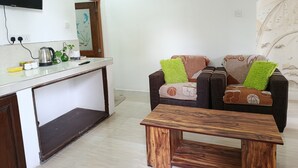 A living room with a sofa, a coffee table, a TV, and a kitchen area with a kettle and a plant. - C&D Ella (Ella)
