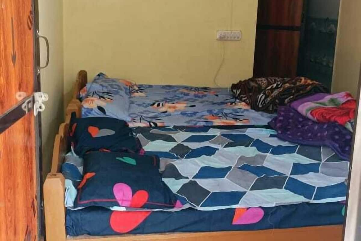 A small, single-bed room with a wooden bed frame, a patterned bedspread, and a colorful rug on the floor.