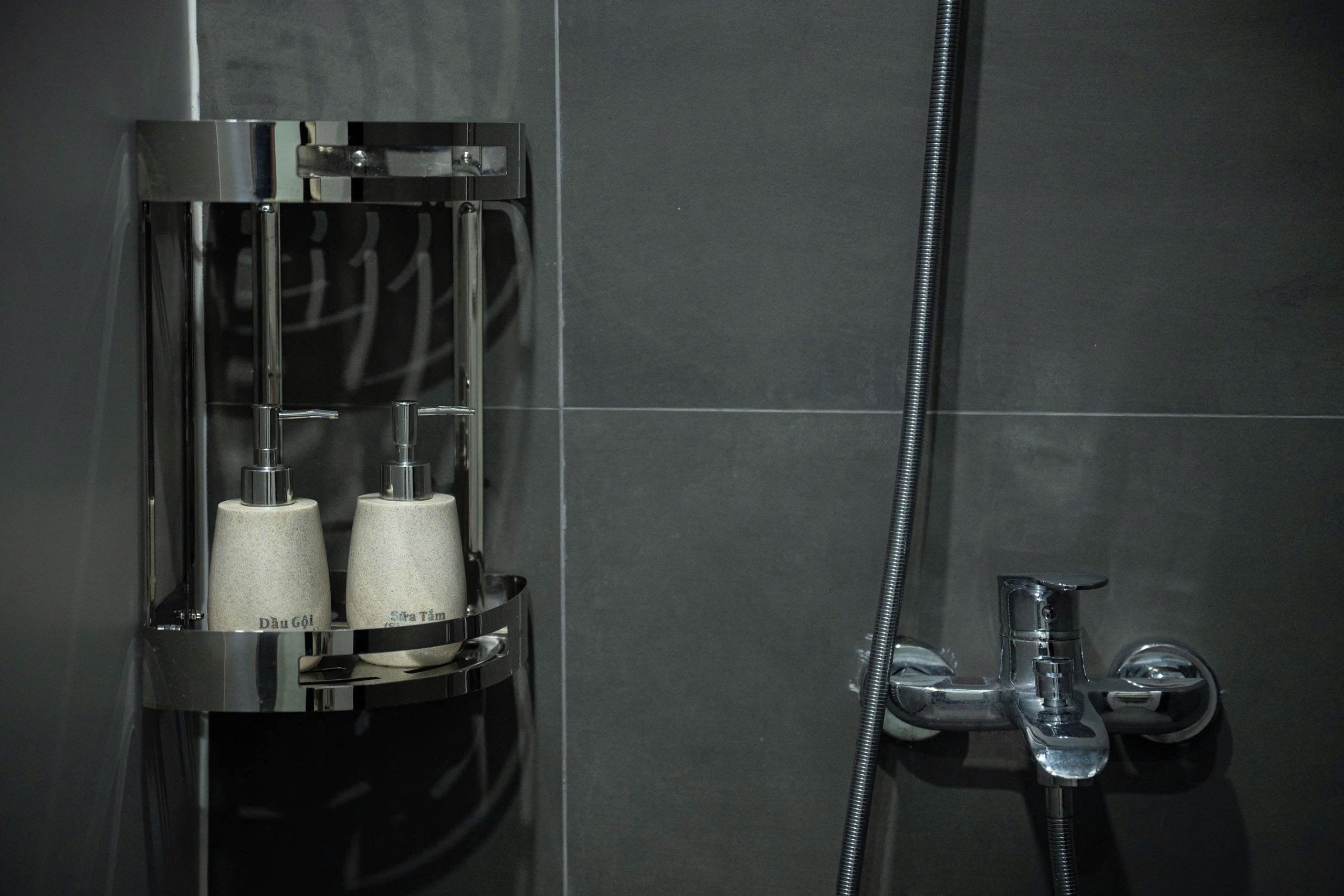 A modern shower enclosure with a chrome finish, a handheld showerhead, and two bottles labeled 'Dau Göl' and 'Sera Tüm' in a transparent holder.