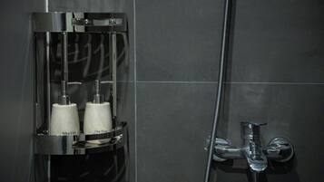 A modern shower enclosure with a chrome finish, a handheld showerhead, and two bottles labeled 'Dau Göl' and 'Sera Tüm' in a transparent holder.