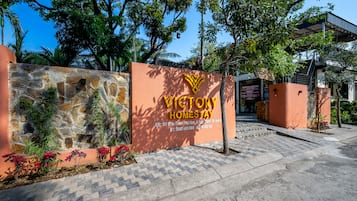 Un mur de pierre avec une enseigne indiquant « Victory Homestay », une allée pavée et un escalier menant à un bâtiment.