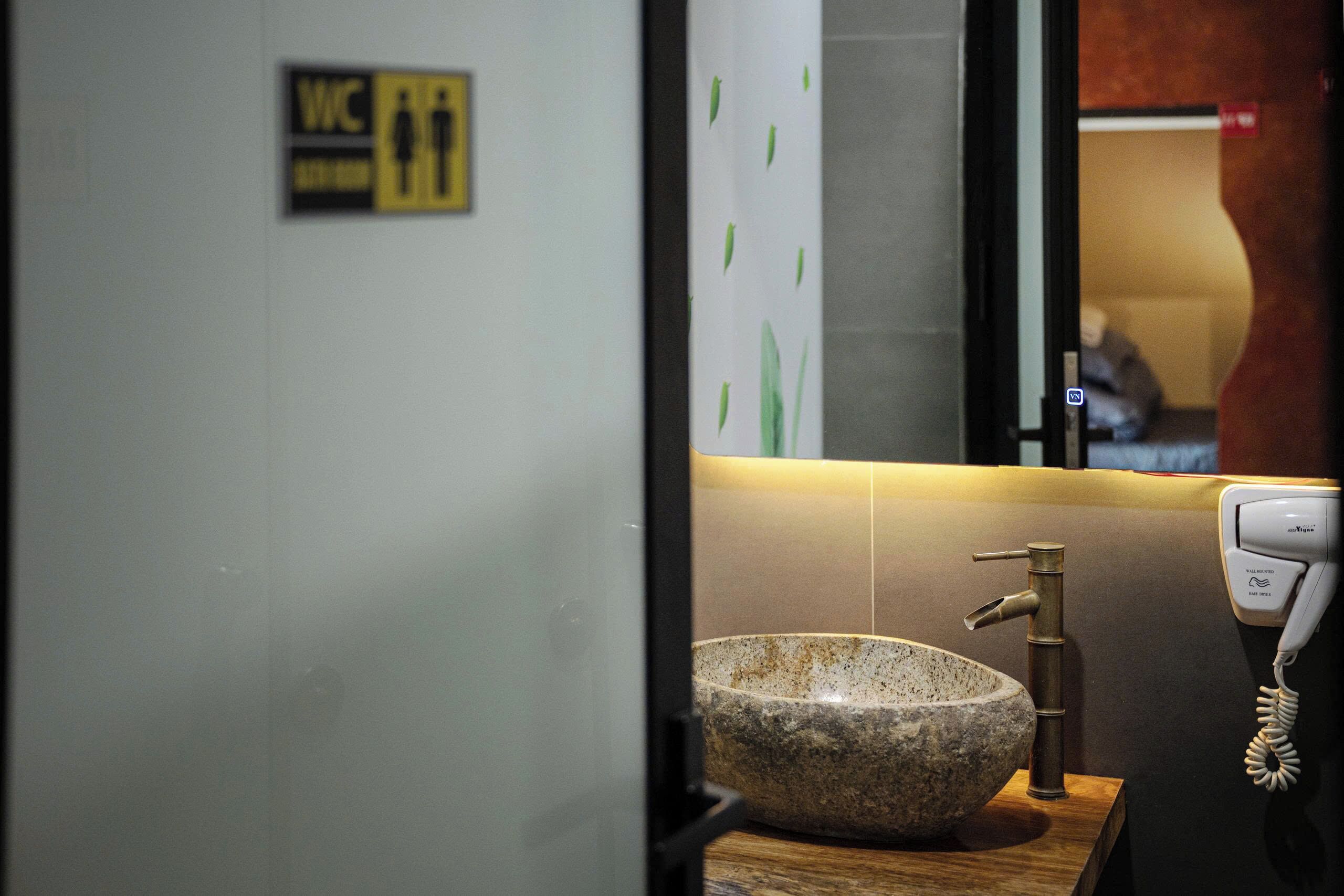 Une salle de bain avec un lavabo en pierre, un miroir, un panneau indiquant les toilettes et un téléphone.
