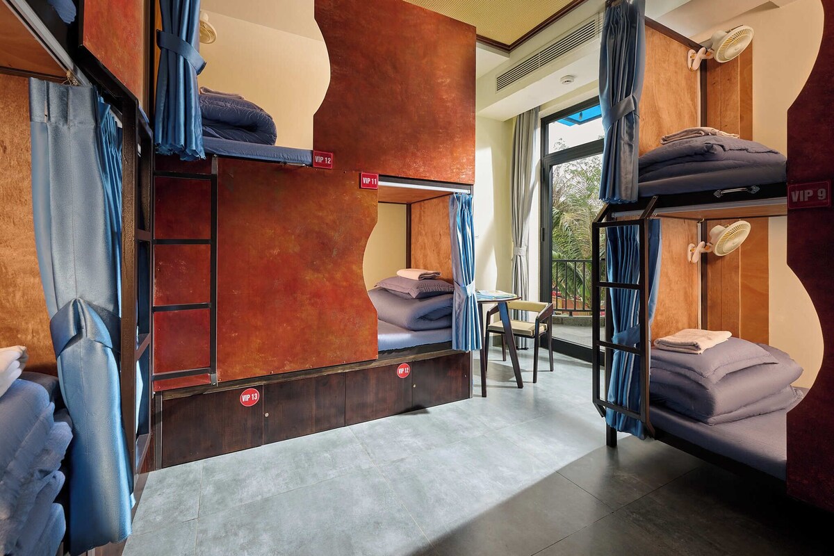 A hostel room with bunk beds, a small table, and a view of the outside.