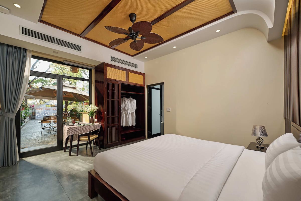 A hotel room with a large bed, a ceiling fan, a table with chairs, and a view of the outside.