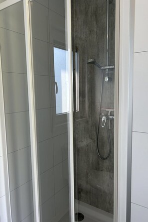 Una ducha a ras de suelo con puerta de vidrio, paredes enlosetadas y una zona de ducha de hormigón.