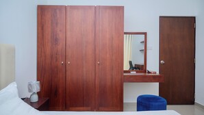 Une chambre à coucher avec un lit, une armoire en bois, un bureau avec un miroir et un tabouret bleu.