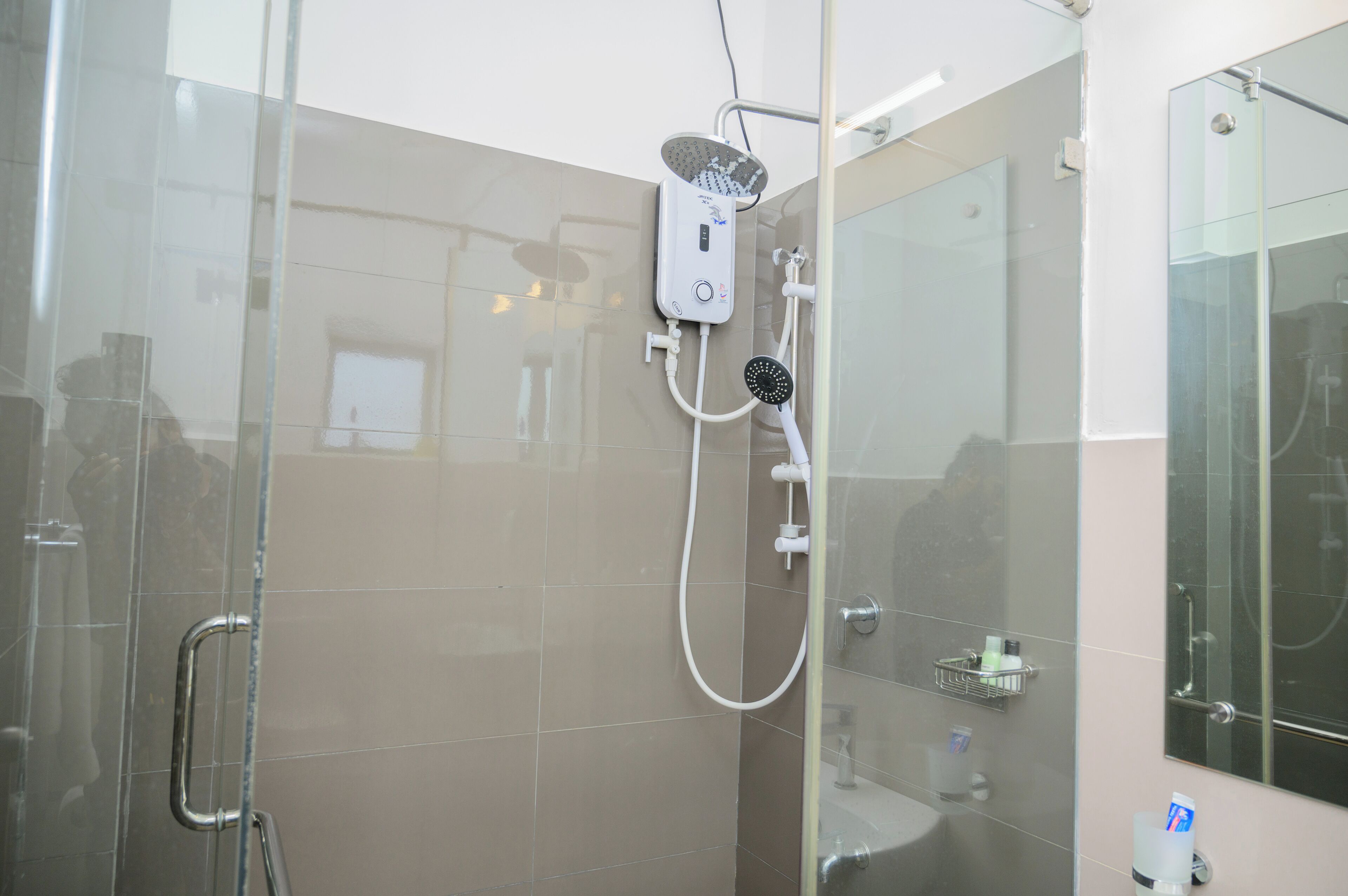 Un baño moderno con cabina de ducha de vidrio, cabezal de ducha manual y masajeador de mano.