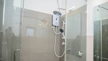 Un baño moderno con cabina de ducha de vidrio, cabezal de ducha manual y masajeador de mano.