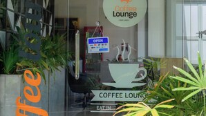 Un café avec une entrée en verre, une enseigne indiquant qu’il est ouvert et un logo représentant une tasse de café.