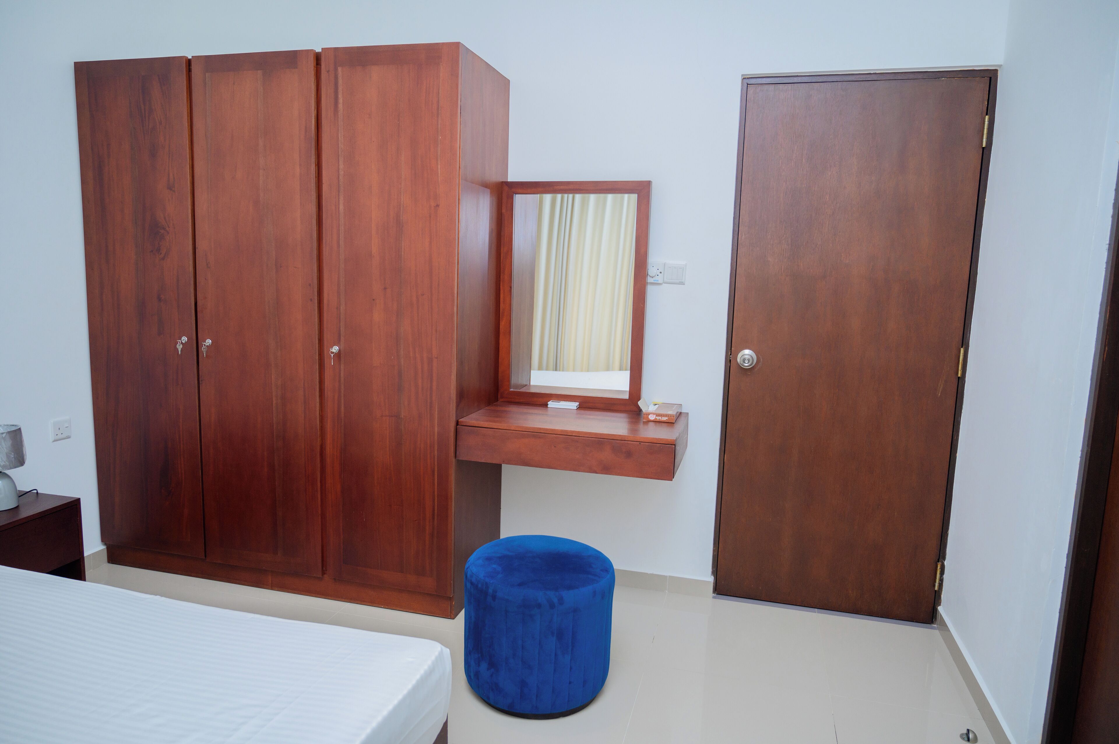 A bedroom with a bed, a wardrobe, a mirror, a door, and a blue ottoman.